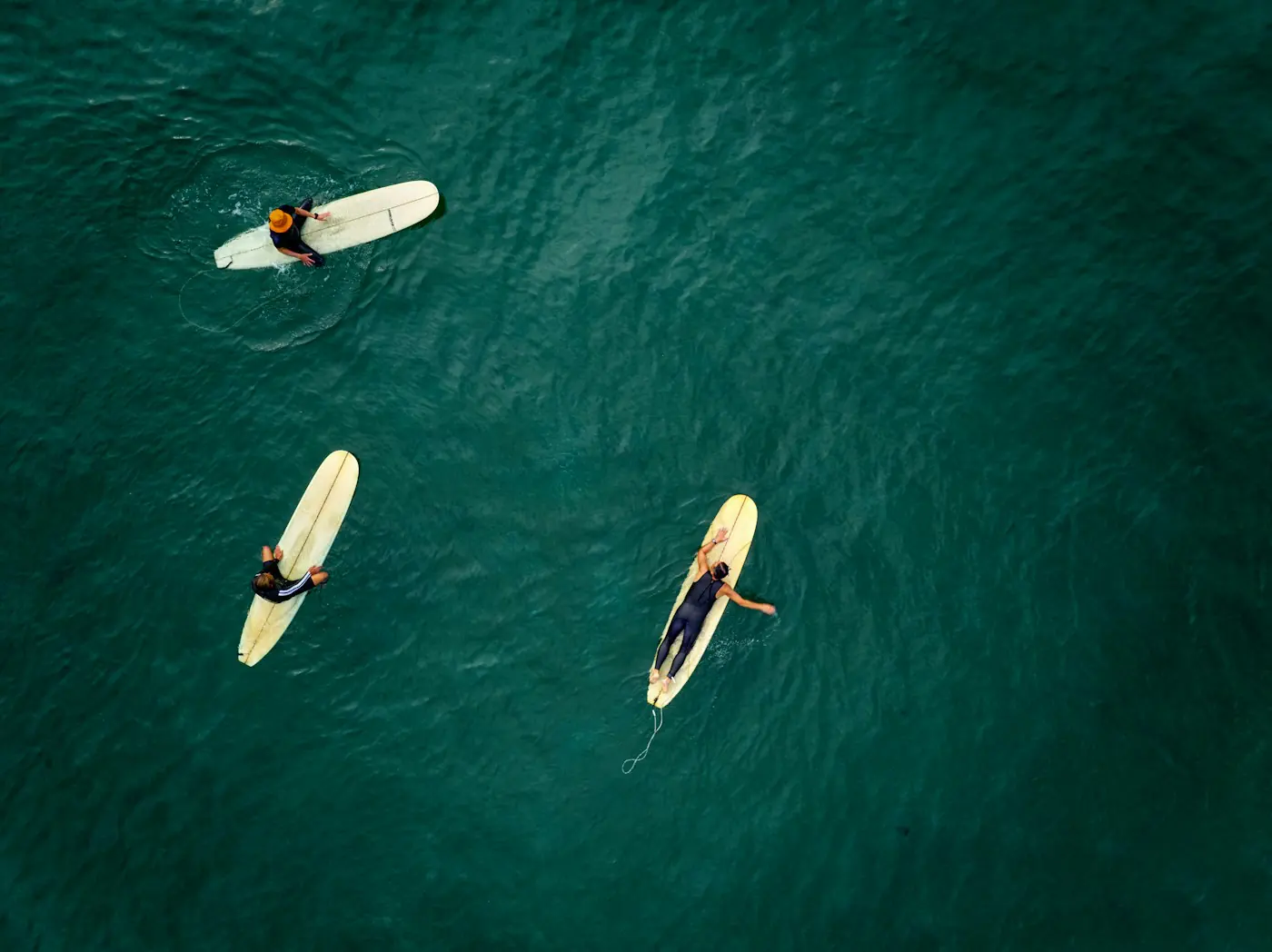 Aerial view of three surfers paddling in deep green water