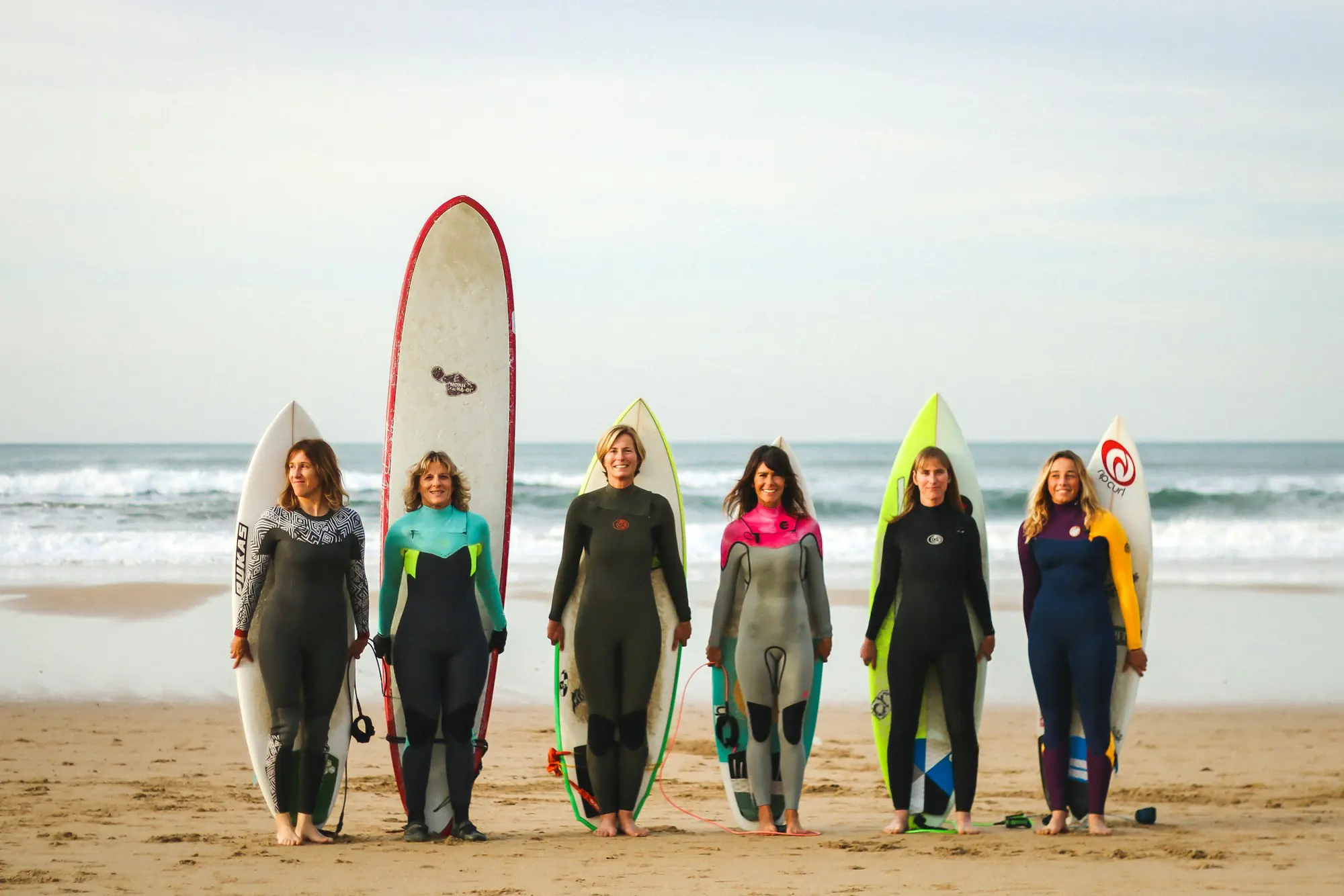 Group of surfers in wetsuits standing with their boards on the beach