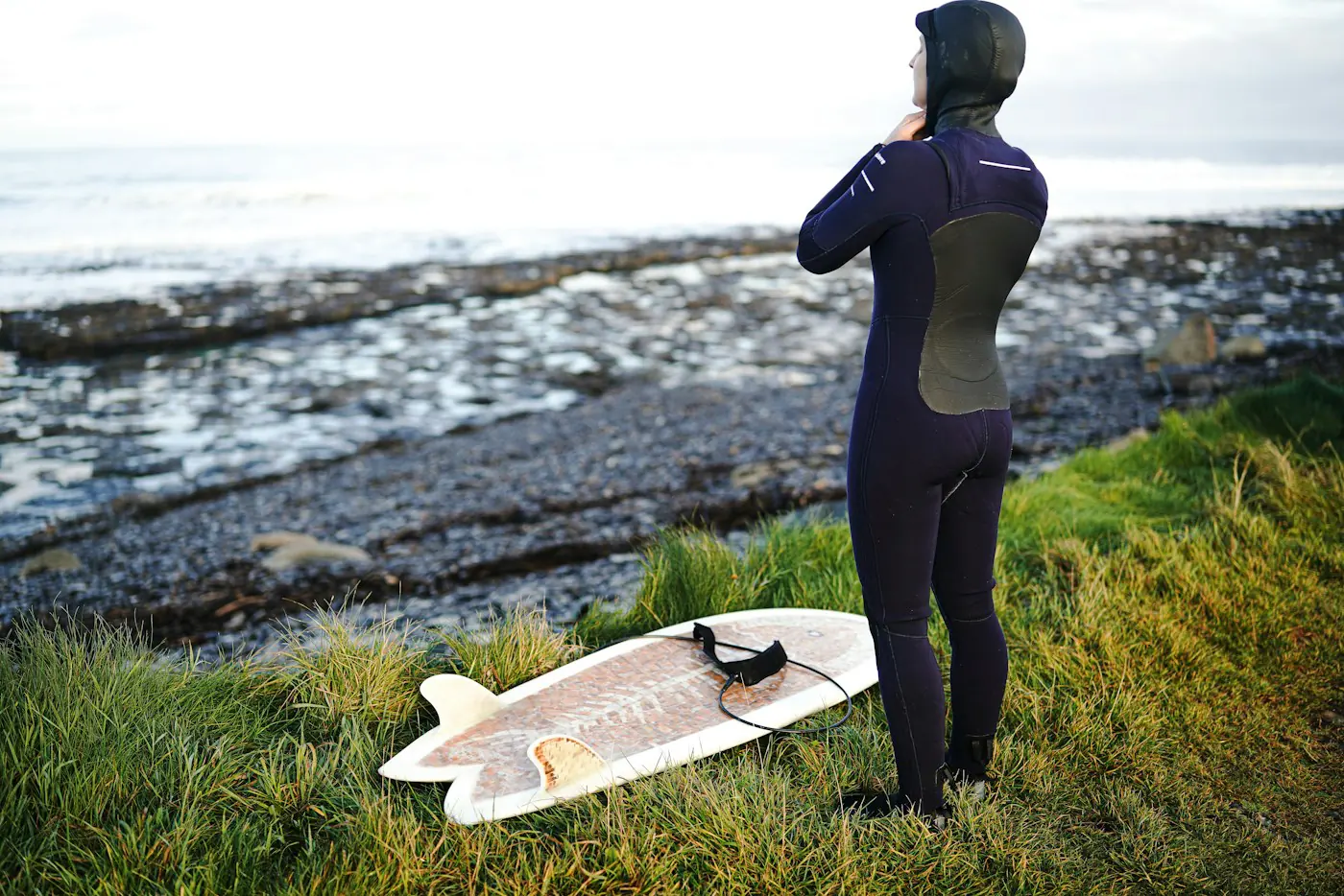 Surfer in a hooded winter wetsuit looking out at the sea