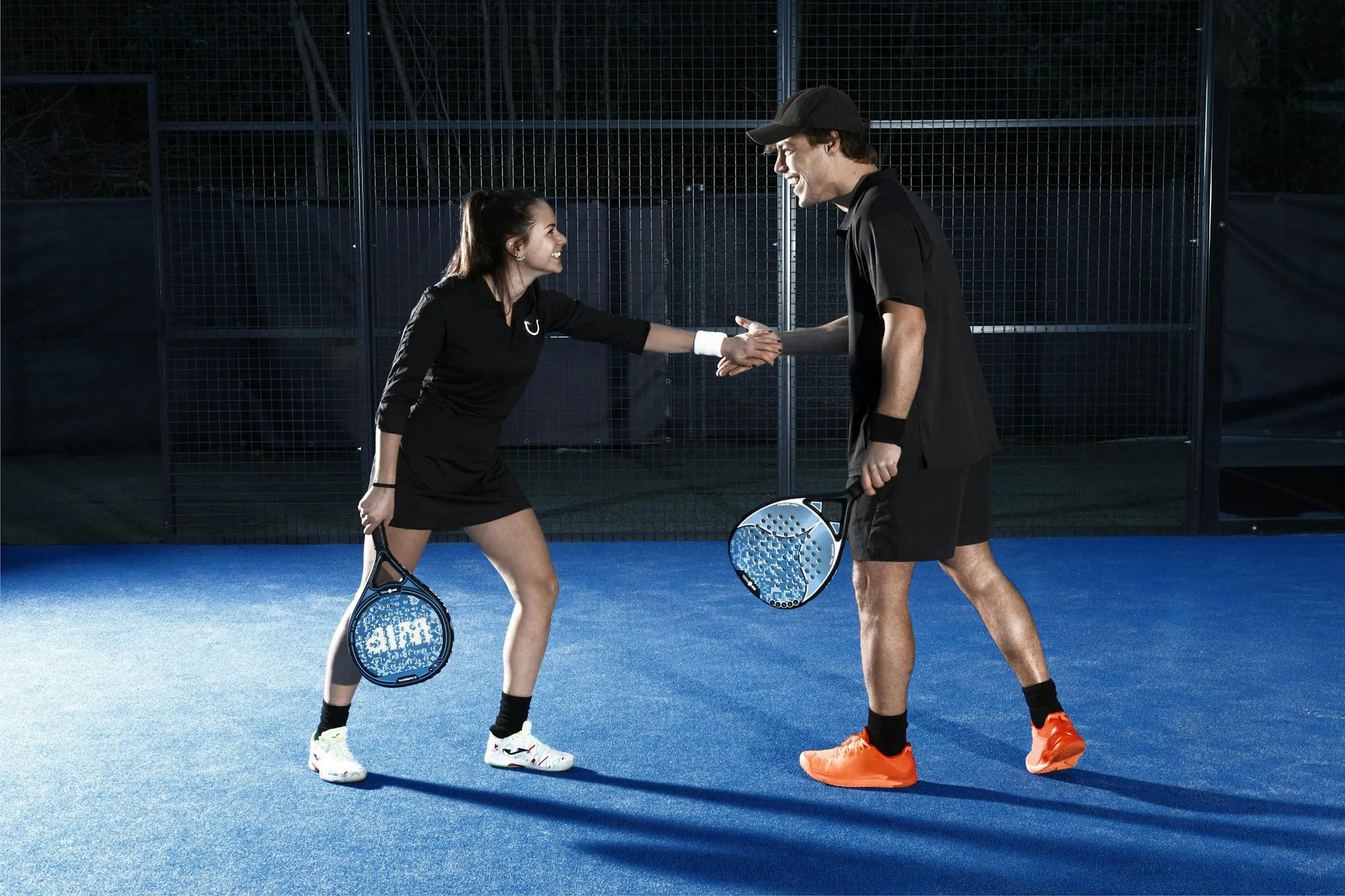 Two padel players shaking hands across a blue court