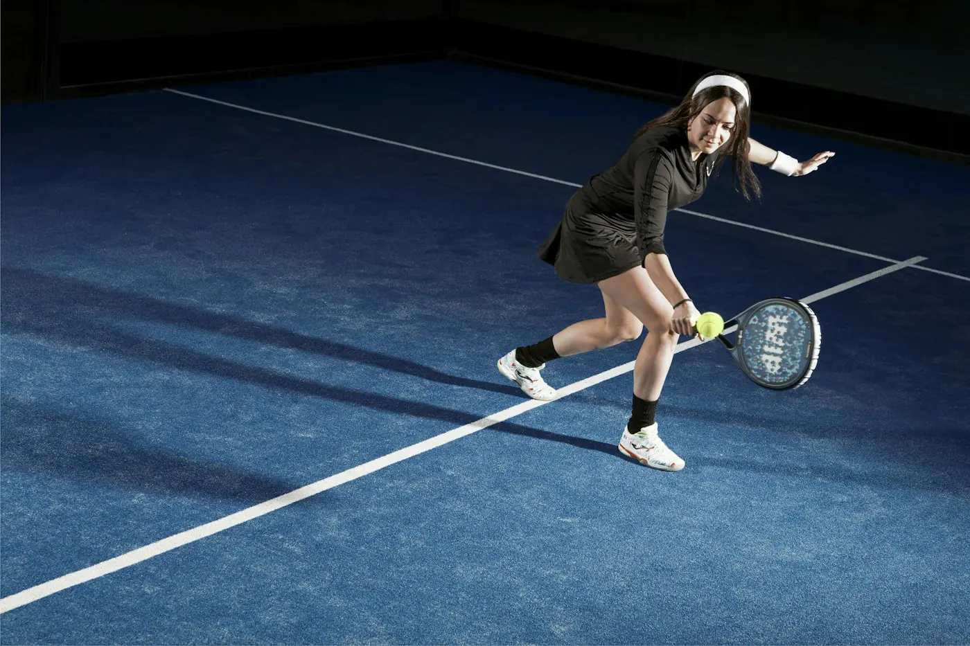 Player returning a low ball on a blue padel court